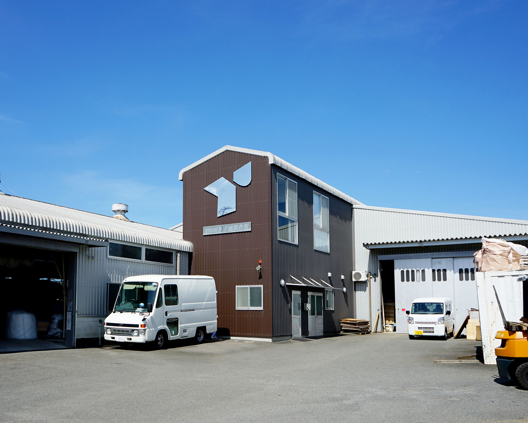 椅子徳製作所の工場外観、茶色と白の建物と配送トラック